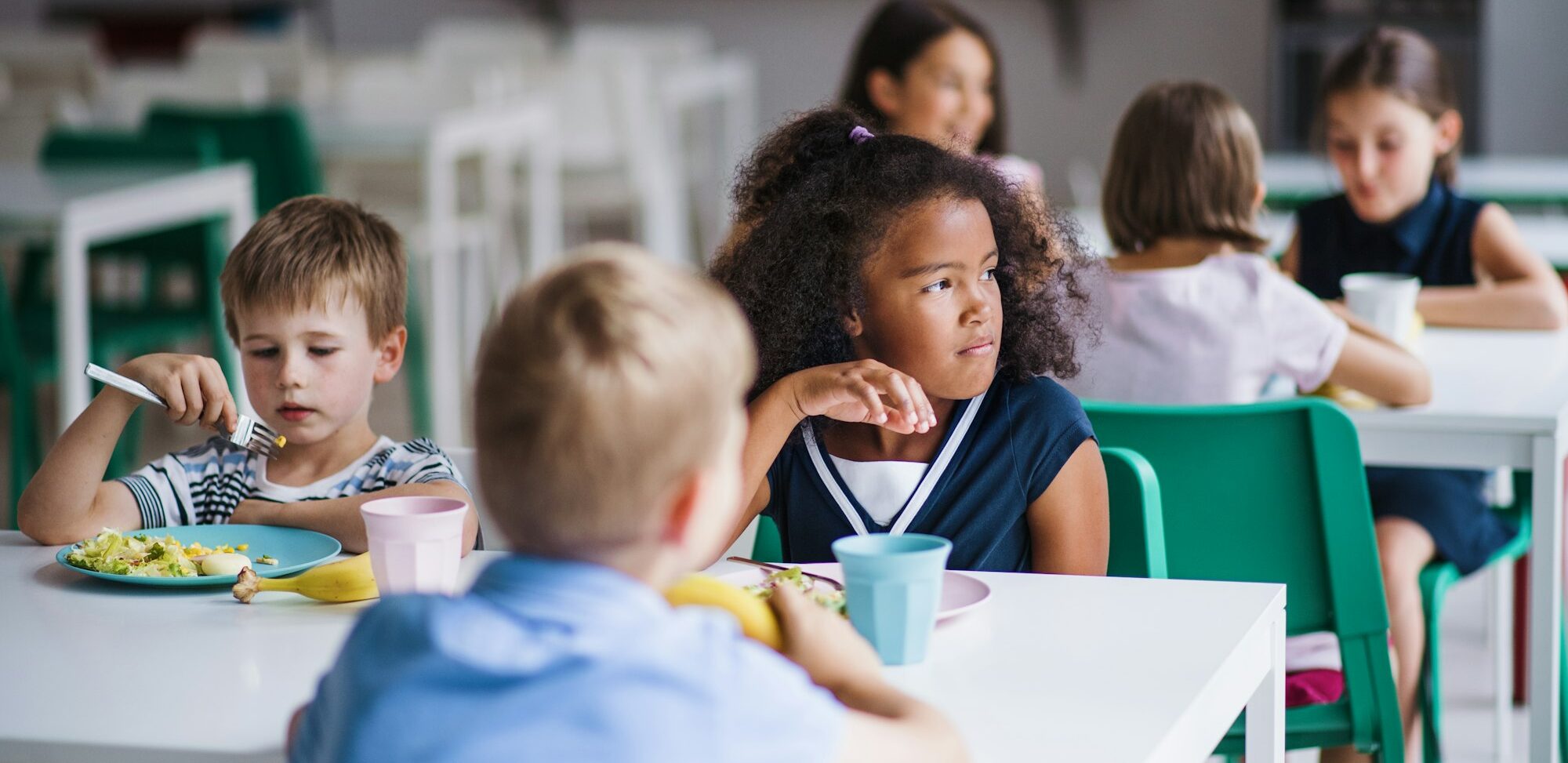 A group of cheerful small school kids in canteen, eating lunch.